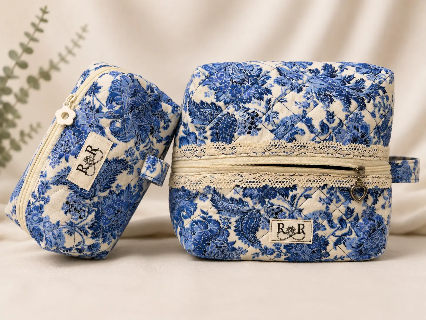 Two coordinating blue and white floral quilted personal care bags with cream zippers, lace trim, and R and R Creative Co labels